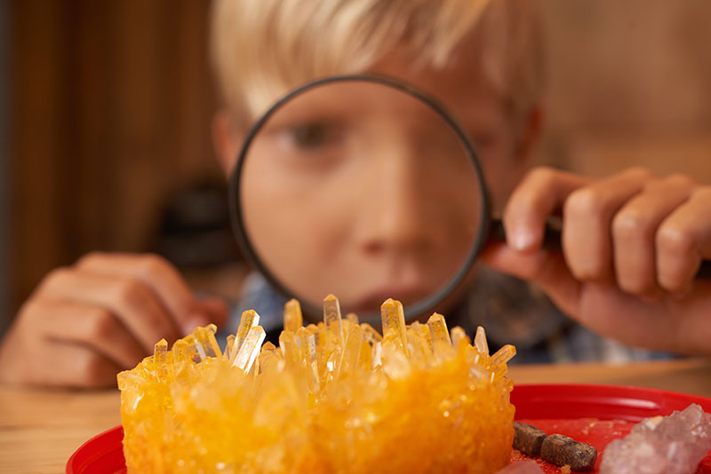 Niño mirando los cristales que cultivó a través de una lupa