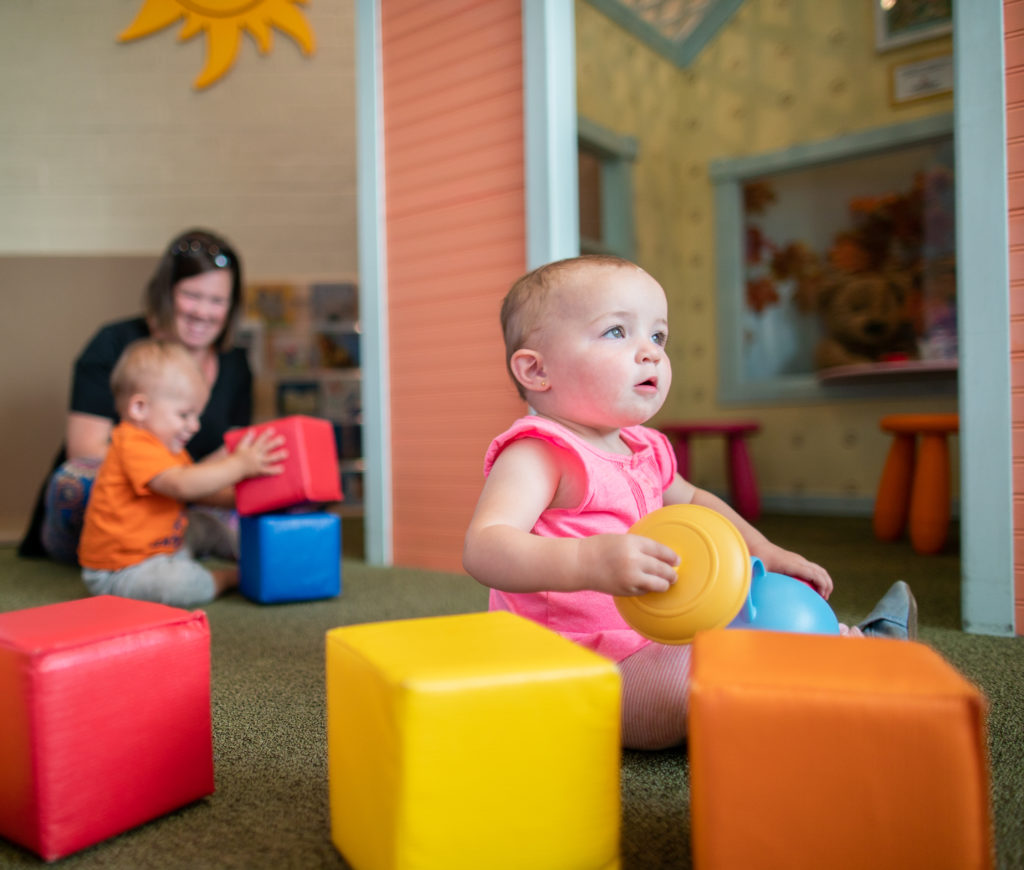 Infant in pink outfit staring in wonder and playing with blocks in totopia
