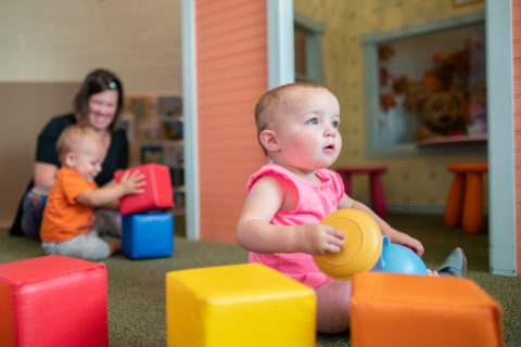 Infant in pink outfit staring in wonder and playing with blocks in totopia