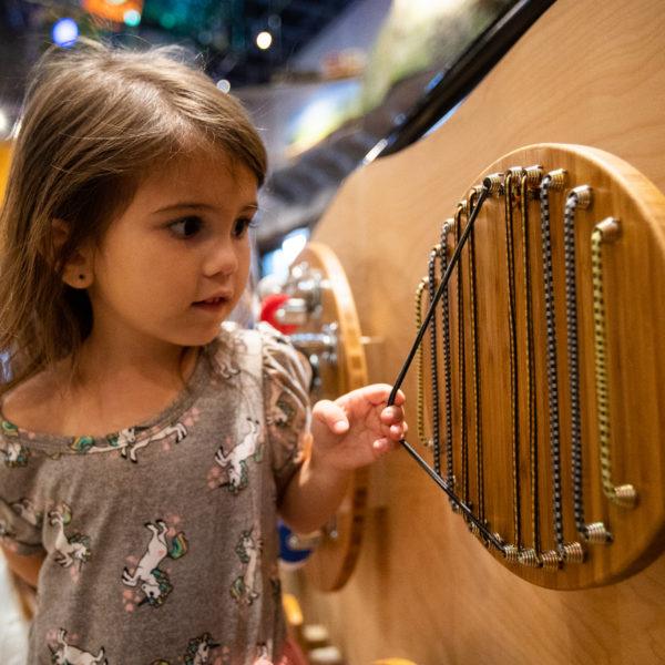 child playing with simple wall exhibit at toddler program