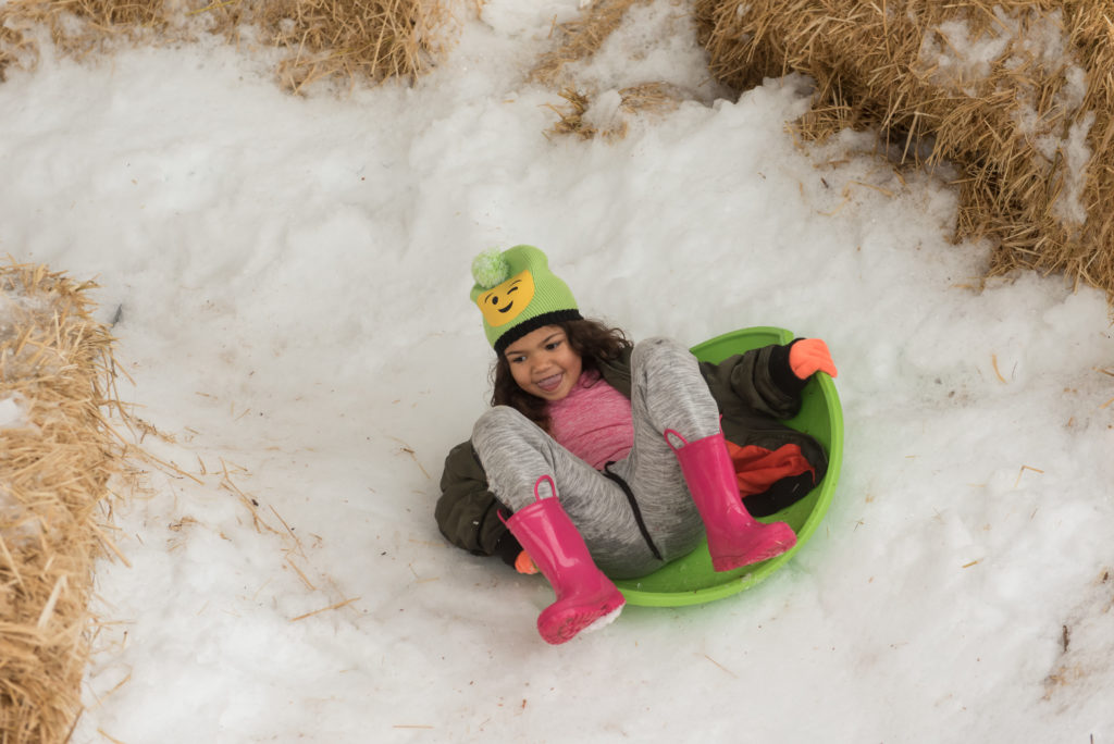 child sliding on snow with plastic sled