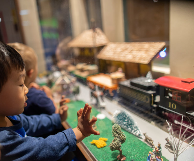 two kids admiring toy trains through a glass partition