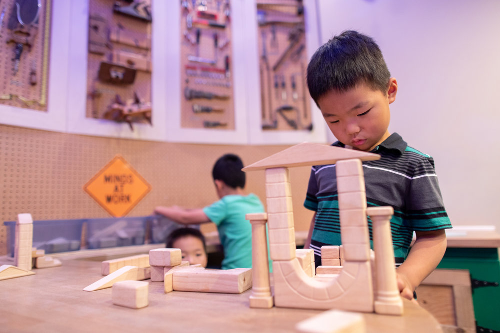 young boy looking at wooden blocks in construction play area