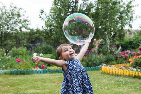 little girl is playing with big bubbles in the backyard