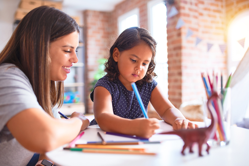 young child with pencil drawing at table supervised by an adult