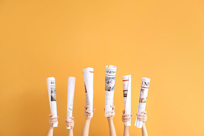 children's hand holding up rolled up newspapers infront of a yellow bckground