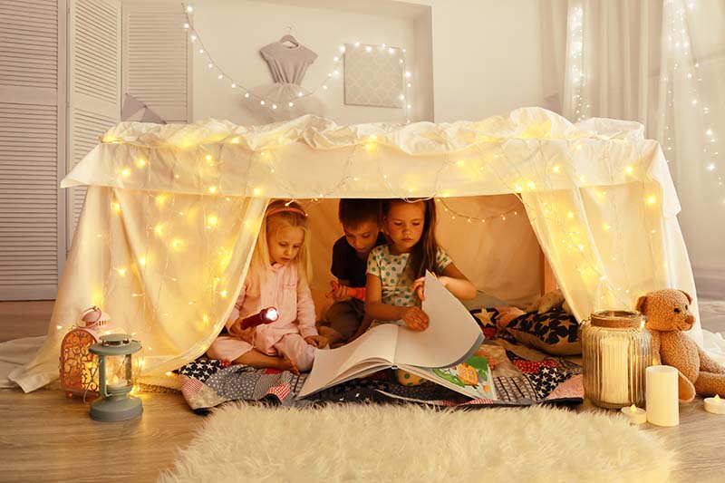 children playing in a indoor fort building made with blankets in their living room