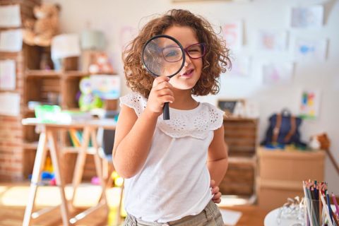 young child in home looking for something with a magnifying glass
