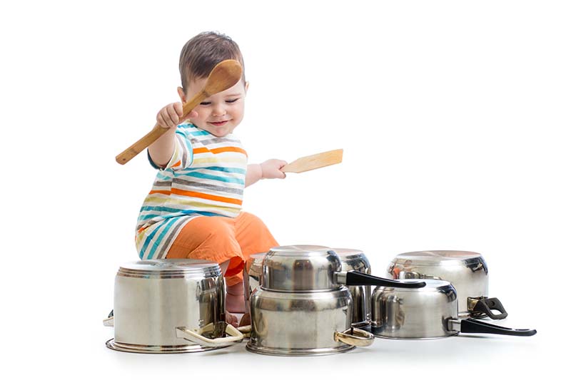 niño que utiliza cucharas de madera para golpear la batería de las sartenes