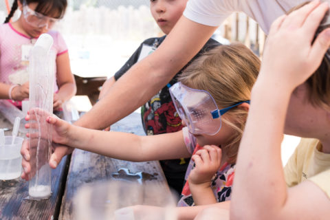 kids with safety goggles on crowding around a fizz rocket science experiment