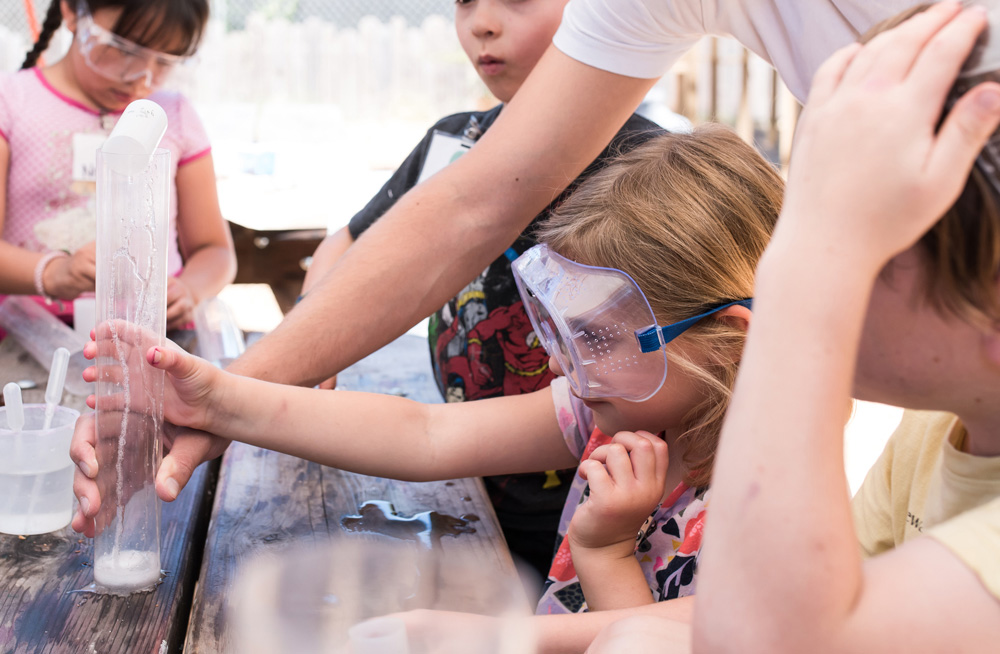 niños con gafas de seguridad en torno a un experimento de ciencia de cohetes de efervescencia