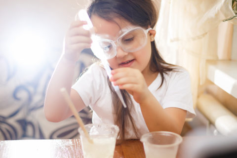 young girl with safety googled on holding a pipette in her hands in the middle of a science experiment