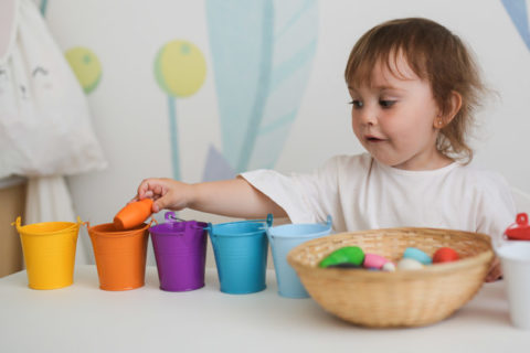 toddler sorting colored objects into cups