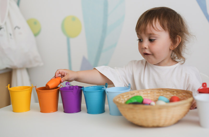 toddler sorting colored objects into cups