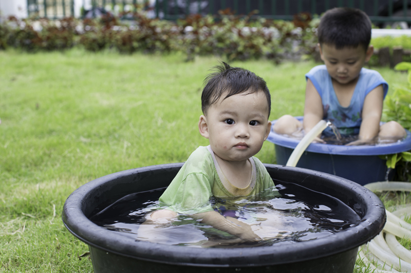 infant sitting in small plastic tub filled with water