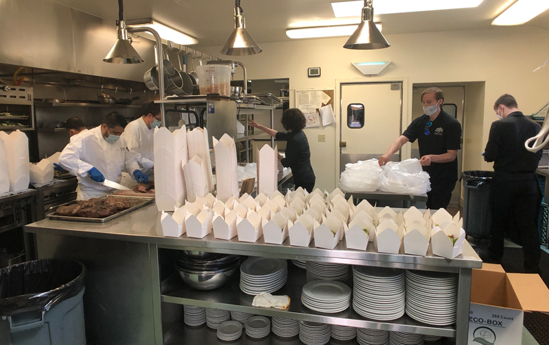 crew packing meals to go in paper containers in kitchen