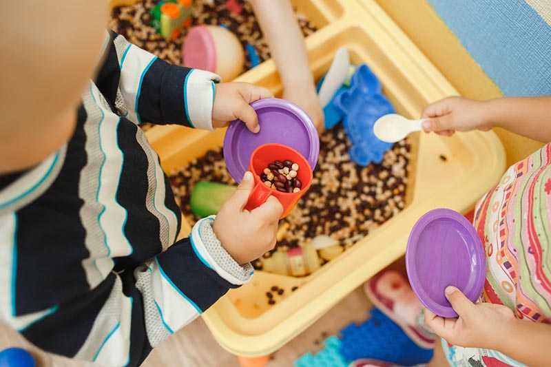 Children play educational games with a sensory bin in kindergarten