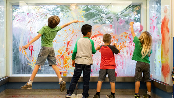 four young boys painting on an art window