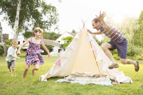 family in backyard with a tent running around in the sunshine playing