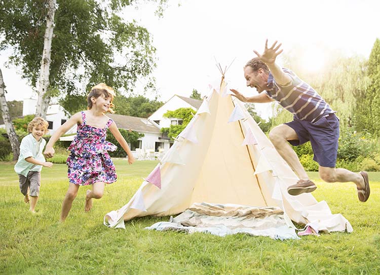 family in backyard with a tent running around in the sunshine playing