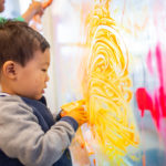 young child fingerpainting on window