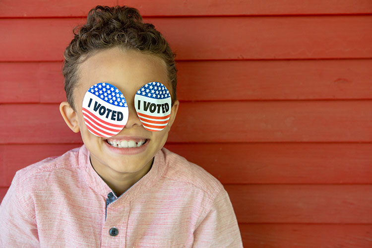 young child smiling wearing I Voted stickers on his face
