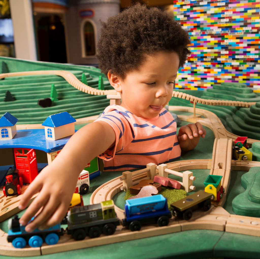 niño jugando con un tren de juguete de madera