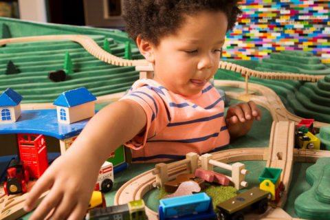 niño jugando con un tren de juguete de madera