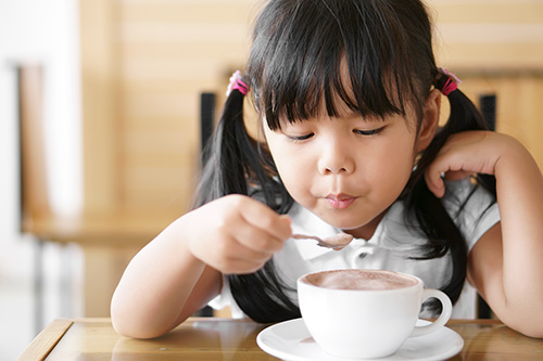 toddler using a spoon to stir and drink a hot chocolate drink