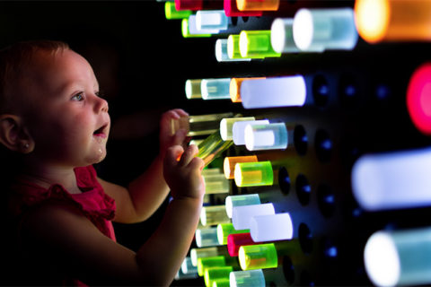 Toddler laying with interactive light peg wall exhibit at the children's museum of sonoma county