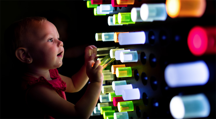 Toddler laying with interactive light peg wall exhibit at the children's museum of sonoma county