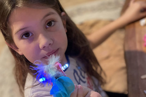 Niña mostrando su accesorio luminoso que hizo después de aprender a crear un circuito eléctrico con la caja de actividades Children's Museum's Electric Bling Kit and Caboodles