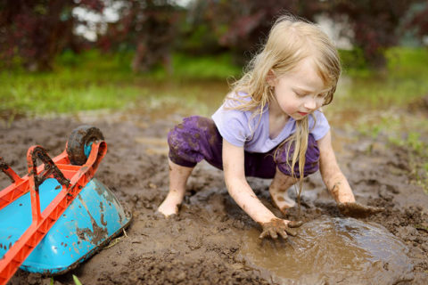 Toddler playing in the mud with a wheel barrel