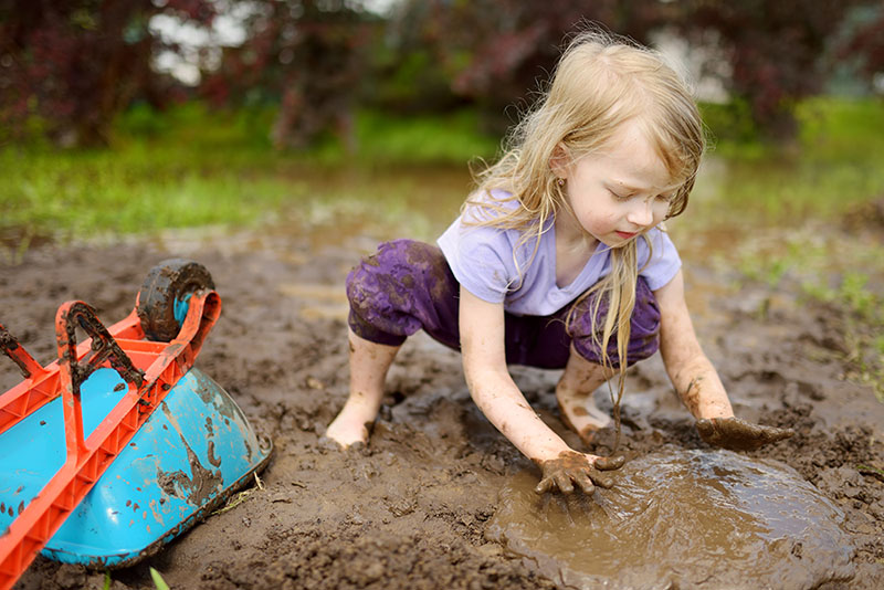 Toddler playing in the mud with a wheel barrel