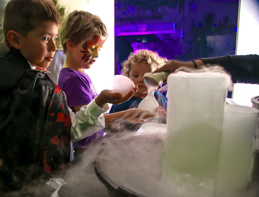 niños con disfraces de halloween haciendo una actividad de vapor de halloween: experimento científico con burbujas de hielo seco