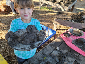 A child holding up a sculpture of a sea lion they made out of mud during the Mud Lab program at the Children's Museum of Sonoma County