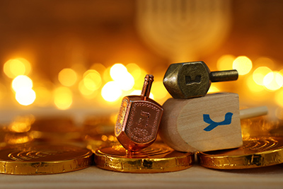 dreidels de madera (peonza) y monedas de chocolate sobre mesa de madera y luces borrosas de fondo