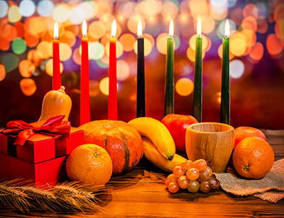 Kwanzaa concepto de vacaciones con decorar siete velas rojo, negro y verde, caja de regalo, calabaza, tazón y fruta con luces borrosas en el fondo