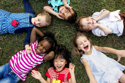 Grupo de niños en edad preescolar tumbados en la hierba en círculo jugando y riendo juntos