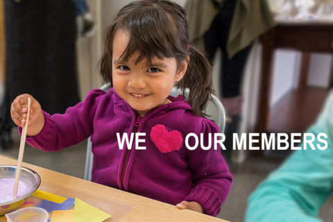 Niña sonriendo y pintando en el Children's Museum of Sonoma County con un texto superpuesto que dice "We love our Members".