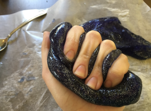 A hand holding and squishing DIY glittery Galaxy Slime