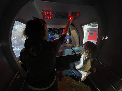 A child and their guardian playing in an interactive space shuttle in the the Space Odyssey exhibit at the Children's Museum of Sonoma County