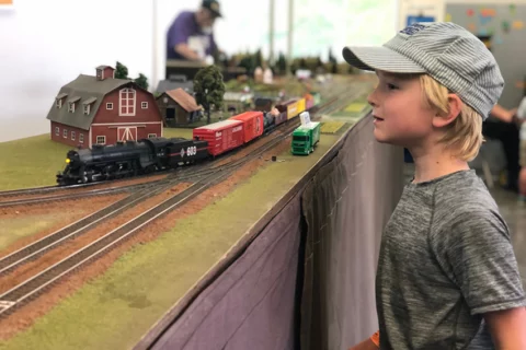 Un niño pequeño con gorra de revisor admirando una maqueta de tren en el evento Great Train Days del Museo de los Niños del Condado de Sonoma.