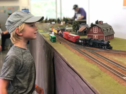 Un niño pequeño con gorra de revisor admirando una maqueta de tren en el evento Great Train Days del Museo de los Niños del Condado de Sonoma.