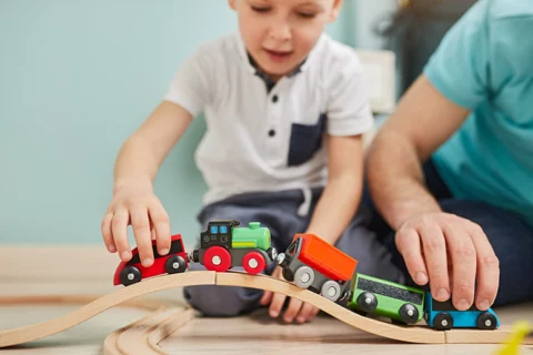 child and father playing with train set at home