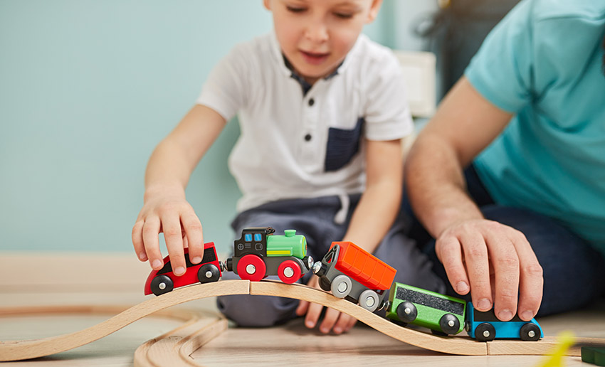 child and father playing with train set at home