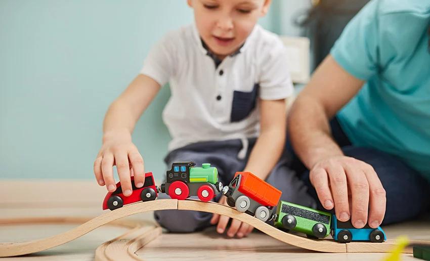niño y padre jugando con el juego de trenes en casa