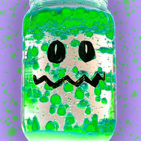 Un Mason Jar con una cara de Monstruo dibujada en él y lleno de burbujas verdes como actividad de Halloween DIY llamada DIY Lava Lamps para niños