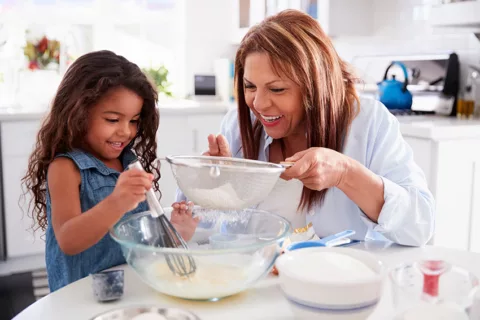 A young girl helping her grandmother mix ingredients in a mixing bowl for a cake they are baking together for the holidays.