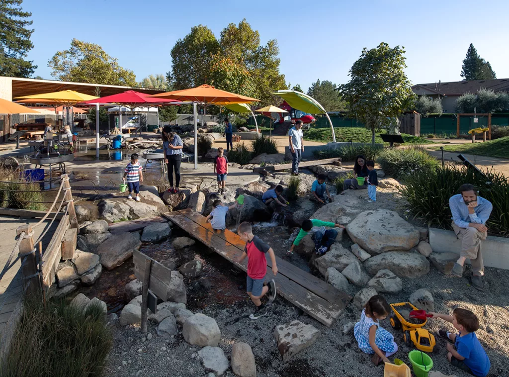 A view of the exterior of the Children's Museum of Sonoma County featuring children and parents playing with interactive exhibits in Mary's Garden.